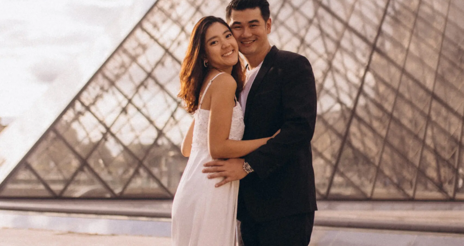 Couple in a white dress and black suit embracing at the Louvre glass pyramid at golden hour, Paris