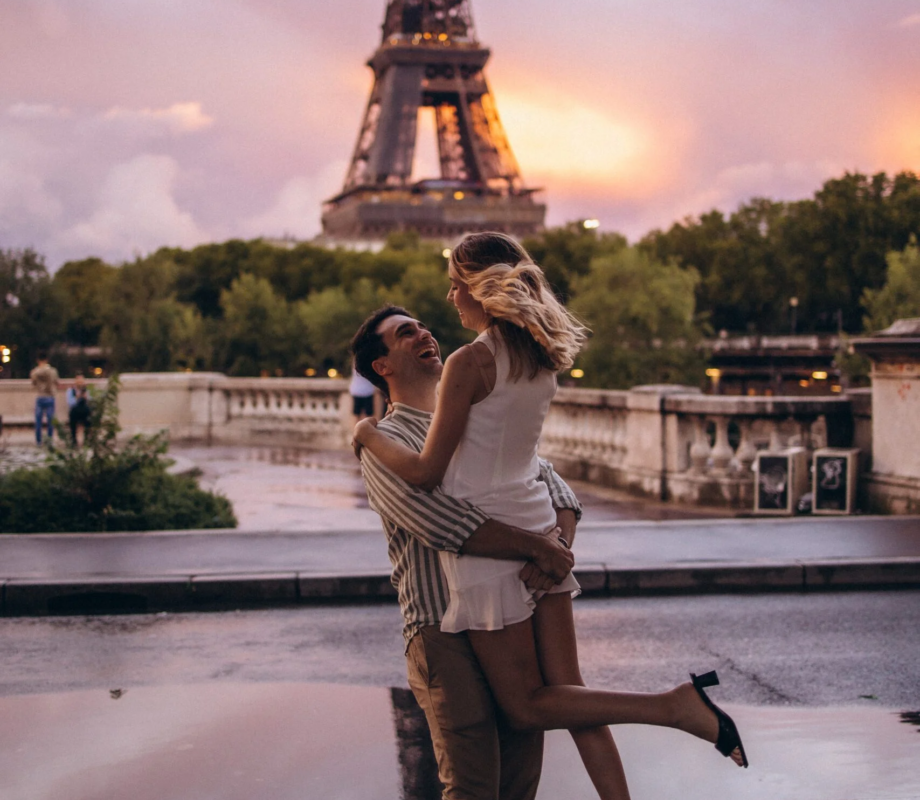 Man lifting his laughing partner at sunset with a pink sky and the Eiffel Tower behind, Paris