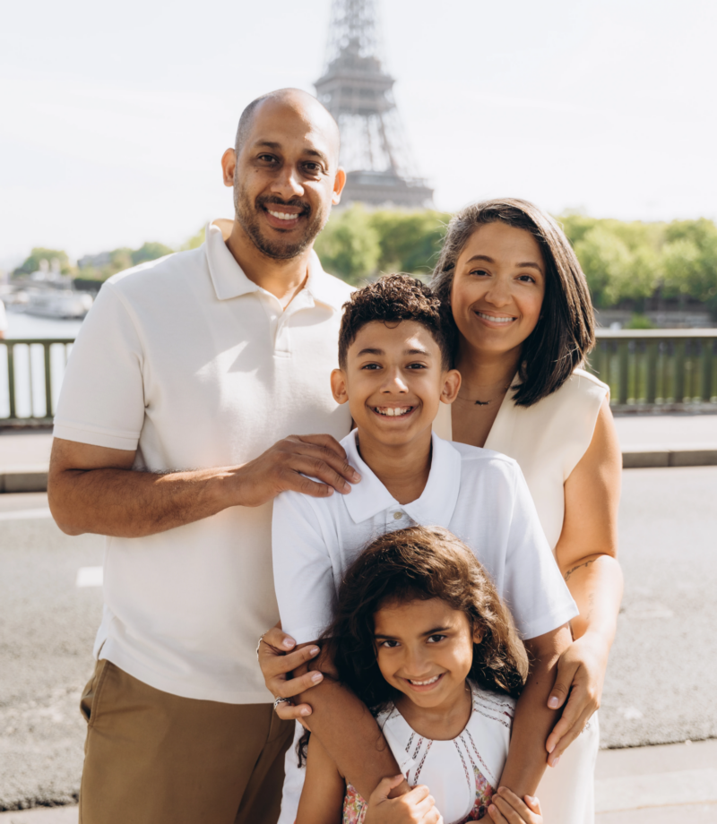 Family hugging and laughing by the Seine with the Eiffel Tower in the distance, Paris