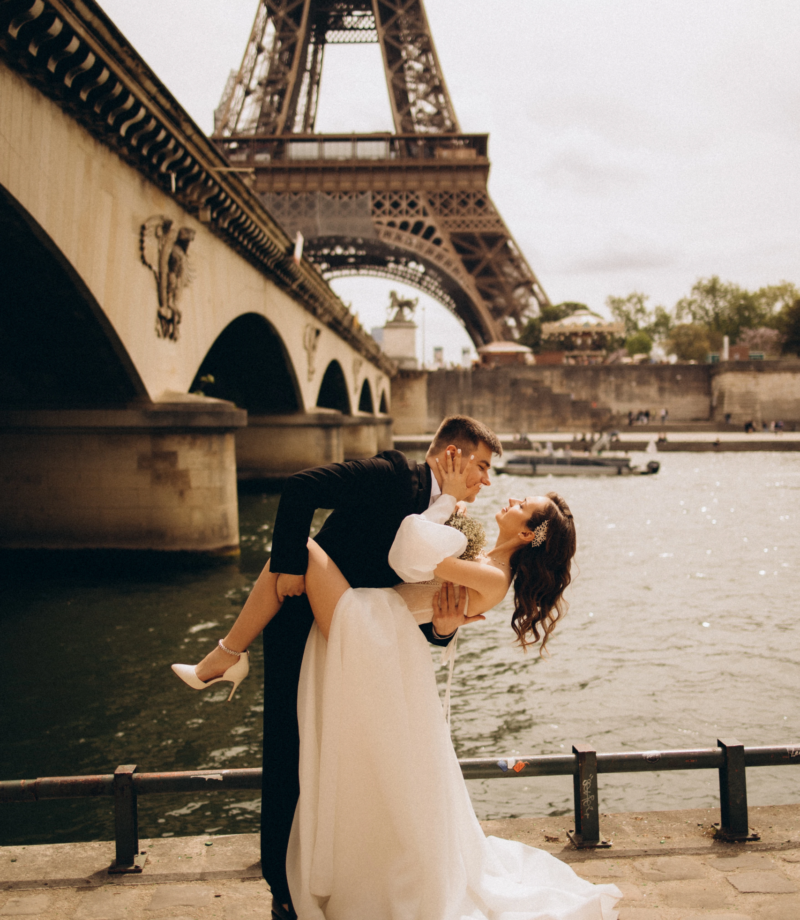 Groom dipping the bride by the Seine under Pont d'Iena with the Eiffel Tower above, Paris
