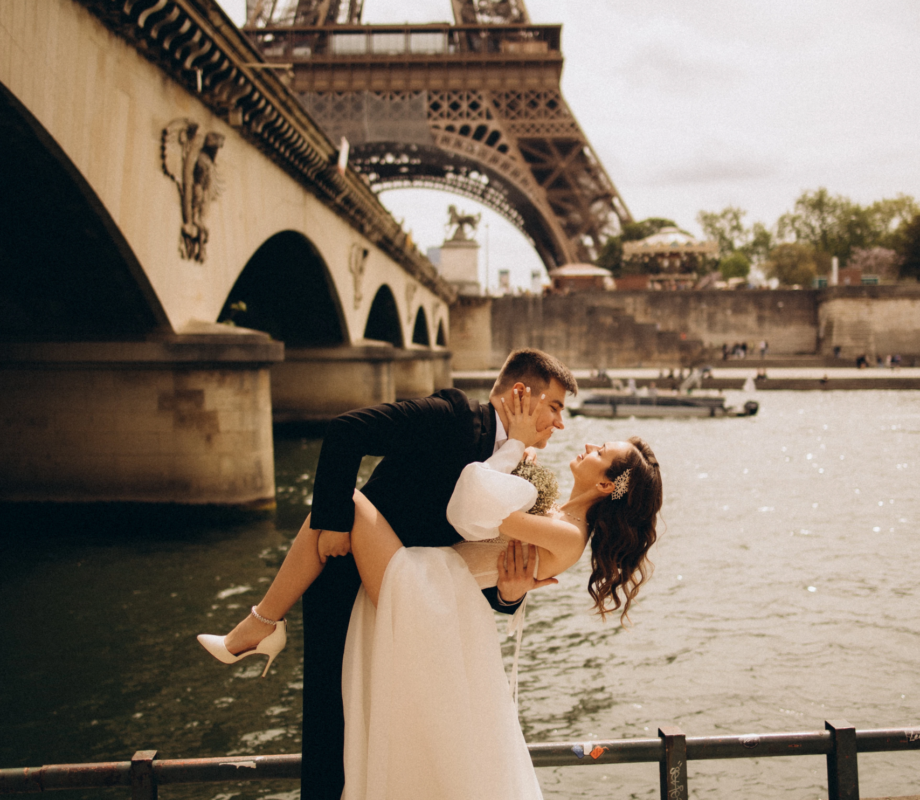 Groom dipping the bride by the Seine under Pont d'Iena with the Eiffel Tower above, Paris