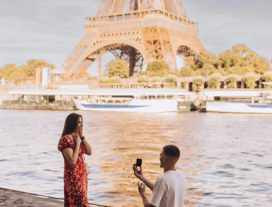 Man on one knee proposing to a woman in a red dress by the Seine with the Eiffel Tower behind, Paris
