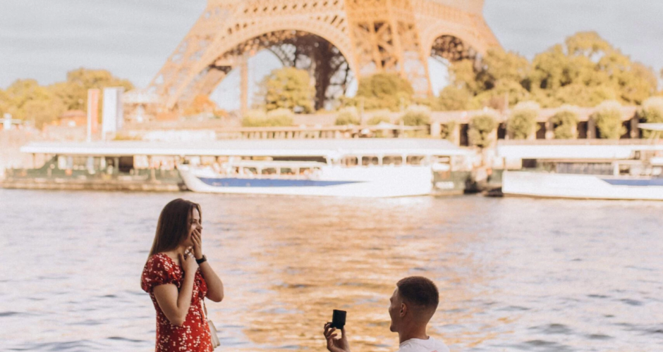Man on one knee proposing to a woman in a red dress by the Seine with the Eiffel Tower behind, Paris