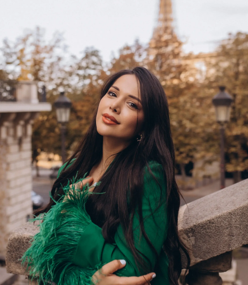 Woman in an emerald feathered blazer leaning on a stone balustrade, Paris