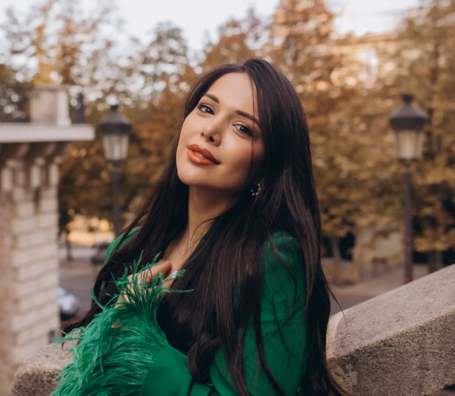 Woman in an emerald feathered blazer leaning on a stone balustrade, Paris