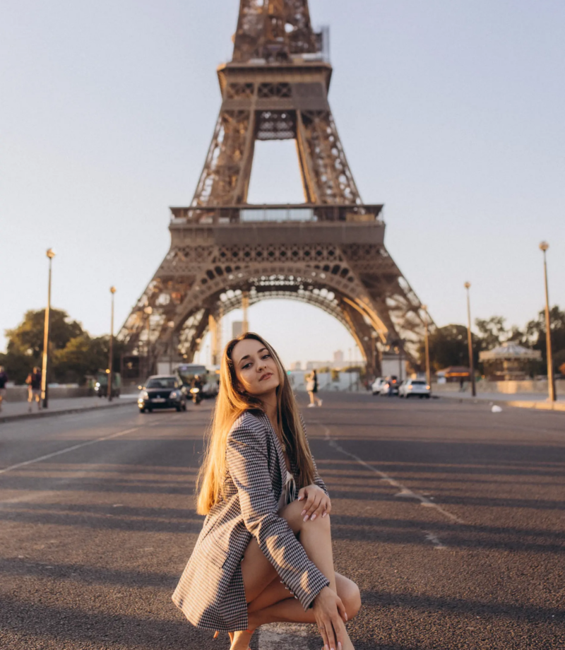 Woman in a checked blazer crouching on an empty avenue at golden hour, the Eiffel Tower behind, Paris