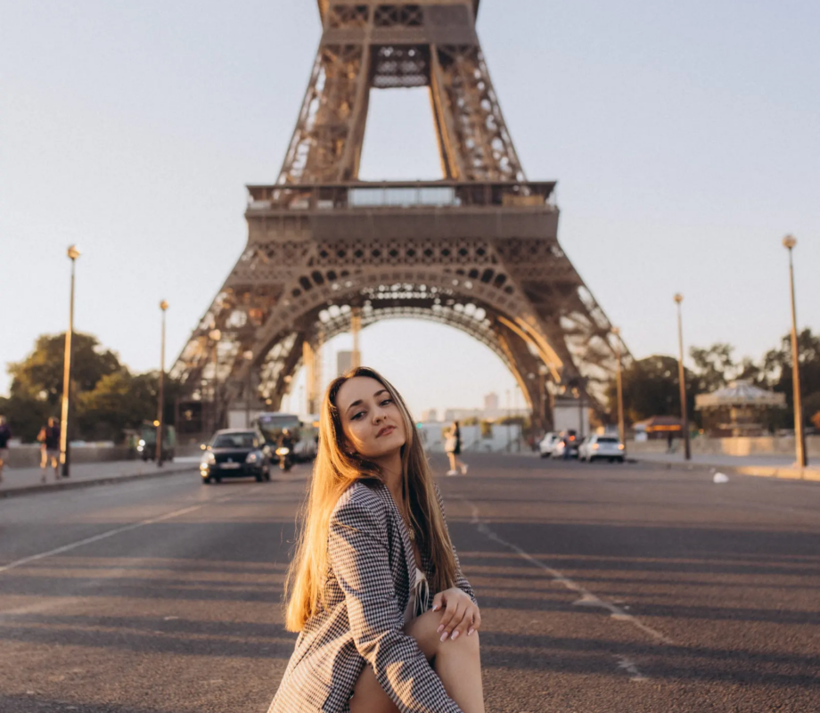 Woman in a checked blazer crouching on an empty avenue at golden hour, the Eiffel Tower behind, Paris