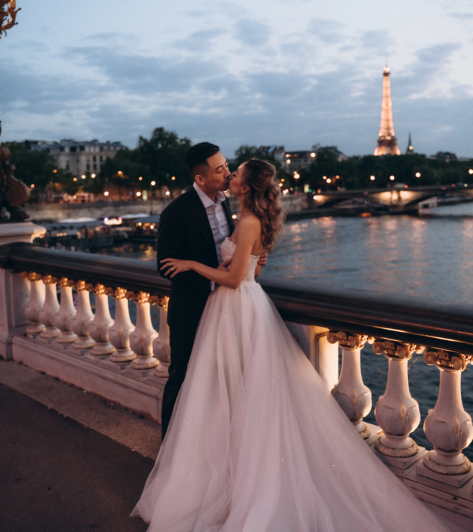 Bride and groom on Pont Alexandre III at dusk with the lit Eiffel Tower across the Seine, Paris