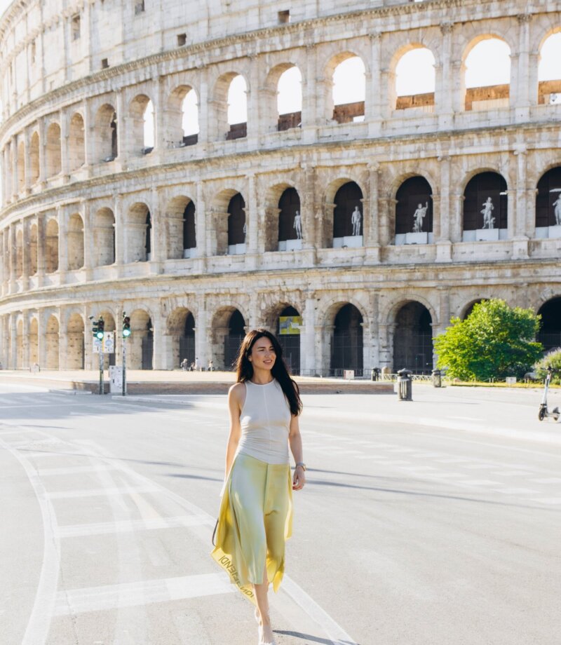 Woman walking down the empty road beside the Colosseum on a June morning, Rome