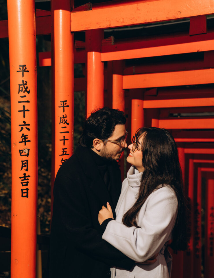 Couple in long winter coats embracing among the red torii gates of Hie Shrine, Tokyo