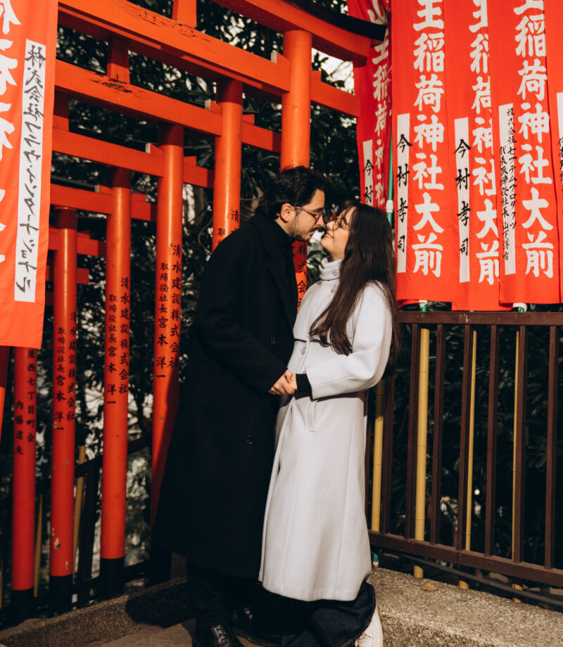 Couple kissing beside red Inari torii gates and shrine banners at Hie Shrine, Tokyo