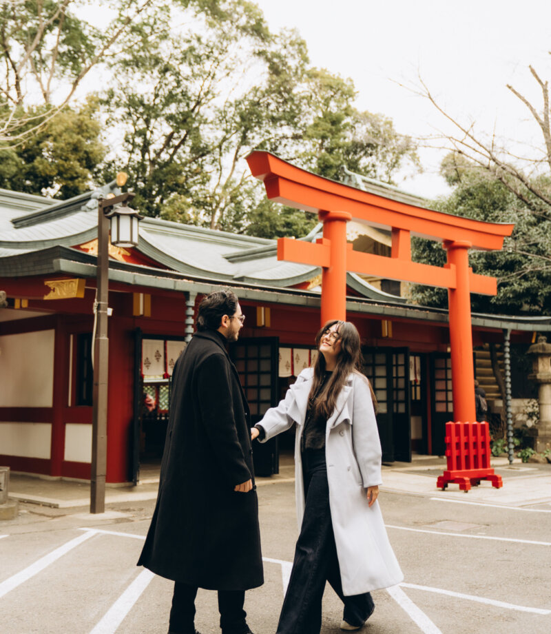 Couple holding hands and walking past a red torii gate in the Hie Shrine courtyard, Tokyo