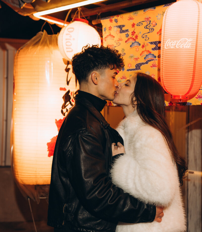 Couple kissing beside large glowing paper lanterns in a Tokyo izakaya lane at night