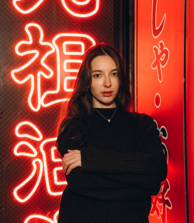 Woman with long dark hair standing against a bright red neon sign on a Shibuya street, Tokyo, at night