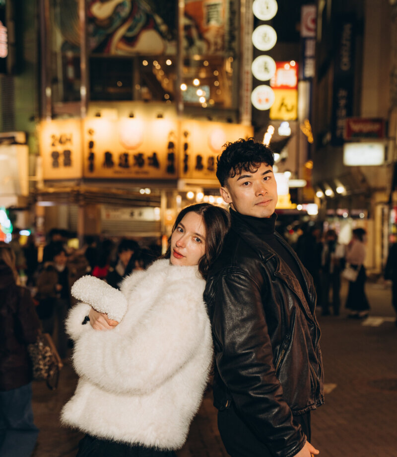 Couple in a white fur jacket and black leather jacket posing on a bright Shibuya street at night, Tokyo