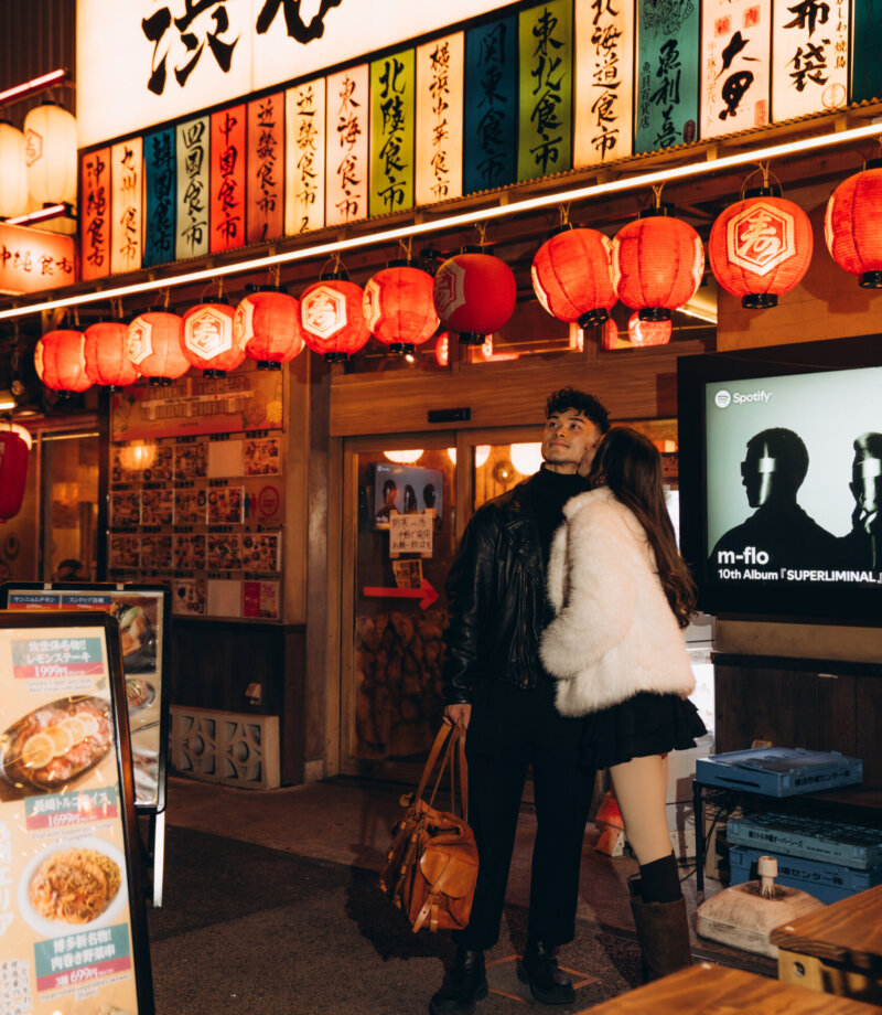 Couple standing under the Shibuya yokocho sign and rows of red lanterns at night, Tokyo