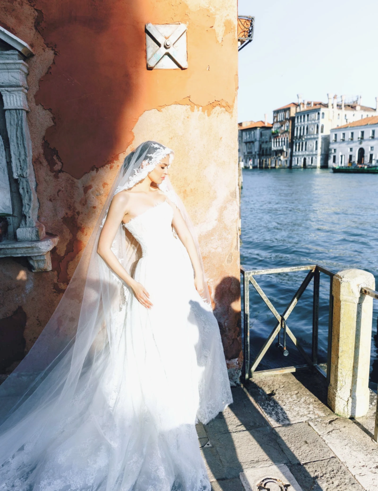 Bride in a long veil against an orange wall on the Grand Canal, Venice