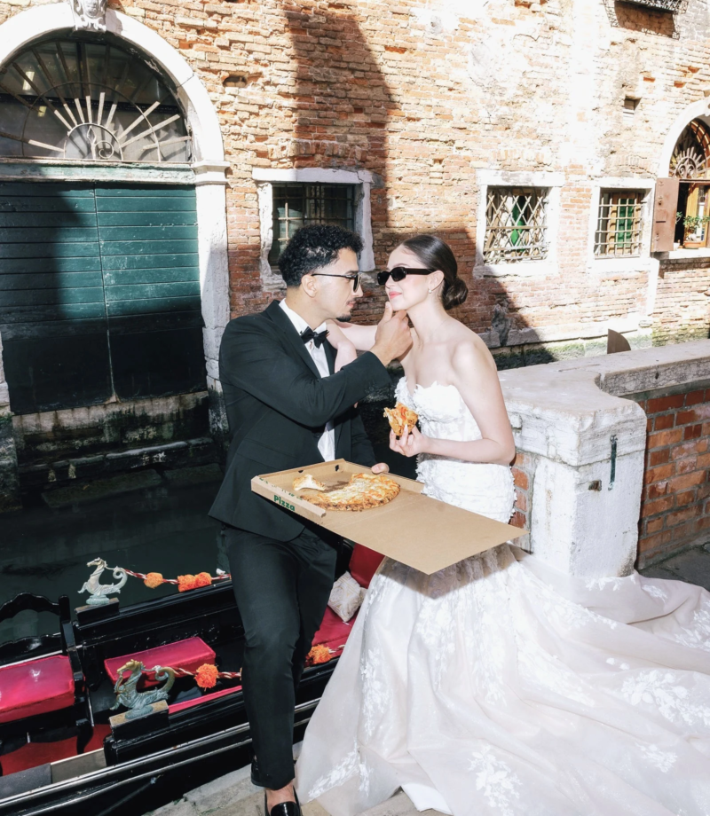 Groom feeding the bride pizza by a gondola landing, Venice
